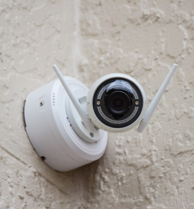 OUR Services white-surveillance-camera-hanging-on-wall-knt4zd8hpb0